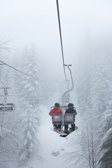 Two snowboarders sitting on the ski chair lift. Ski lift in the forest. Extreme snow conditions....