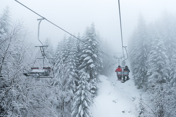 Two snowboarders sitting on the ski chair lift. Ski lift in the forest. Extreme snow conditions, Korbielow village, Poland