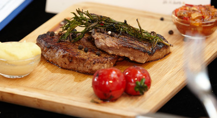 Grilled  beef steak served on wooden board with rosemary,black peppe  and grilled tomatoes.