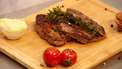 Grilled  beef steak served on wooden board with rosemary,black peppe  and grilled tomatoes.