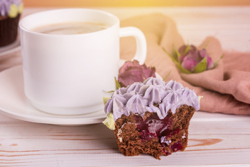 Chocolate delicious cupcake with cream and fragrant coffee with milk on a white wooden table.