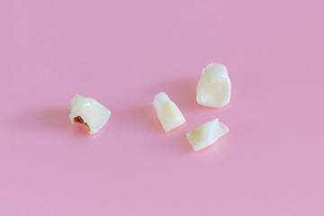 Three healthy and one caries-damaged baby teeth lie on a light pink background