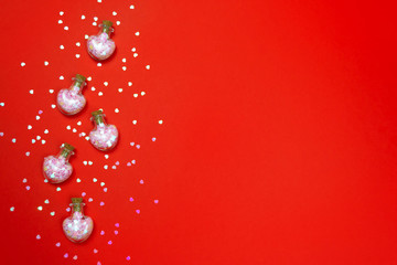 Five bottles with pink glitter holographic confetti hearts on red background. Valentines Day Flat lay composition. Glass container potion concept. Love symbol romantic banner template, copy space