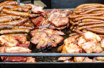 Street food, cooking pork steaks and sausages on grill