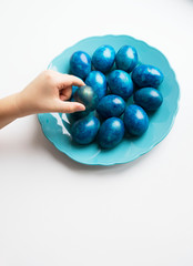 blue eggs laid out in a plate on the table for Easter. A child holds an Easter egg in his hands