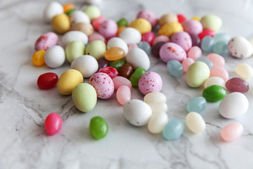 Happy Easter concept. Preparation for holiday. Easter candy chocolate eggs and jellybean sweets on trendy gray marble background. Simple minimalism flat lay top view copy space.
