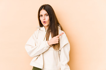 Young caucasian woman isolated on beige background smiling and pointing aside, showing something at blank space.
