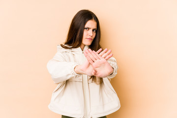 Young caucasian woman isolated on beige background standing with outstretched hand showing stop sign, preventing you.