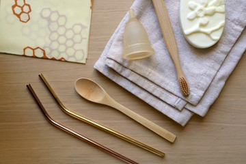 Fototapeta na wymiar Various zero waste products on a wooden table: cloth, soap, cutlery, straws, toothbrush and menstrual cup. Top view.