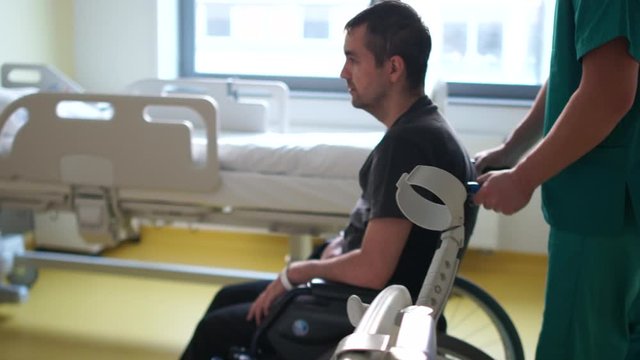 Young man with disabilities gets up from a wheelchair in a hospital. A nurse helps him. Recovery and rehabilitation after a stroke, rehabilitation after a car accident