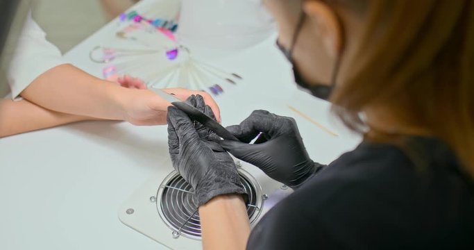 Manicurist processes the nails of the client, gives shape with a nail file. Modern nail studio. Close-up.