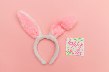 Happy Easter concept. Preparation for holiday. Inscription HAPPY EASTER letters decorative bunny ears isolated on trendy pastel pink background. Simple minimalism flat lay top view copy space.