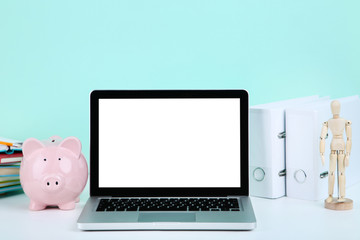 Laptop computer with piggybank, folders and wooden figure on blue background