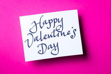 Handwritten Happy Valentine's Day message in simple calligraphic script on white card sitting on bright pink background