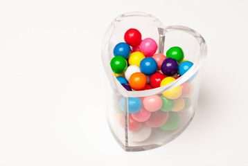 Clear heart-shaped candy jar filled with bright, colorful Valentine gumball candies on white background