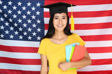 Young woman in graduation cap holding books on American flag background