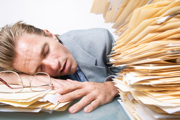 Tired office worker sleeping next an overwhelming stack of paperwork on his desk