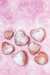 Homemade heart sheped donuts with powdered sugar on pnk background. Tasty doughnuts on cute pink pastel background
