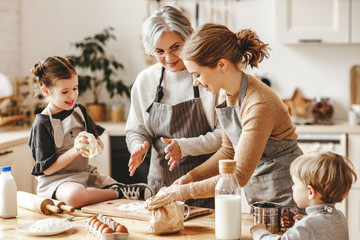 happy family a grandmother with her daughter and grandchildren cooks in kitchen, kneads dough,...