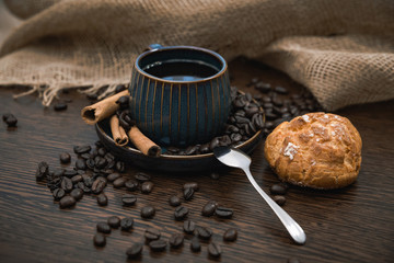 cup of coffee with cinnamon sticks, bun and canvas on brown table
