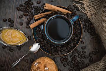cup of coffee with cinnamon sticks, orange jam and bun on brown table