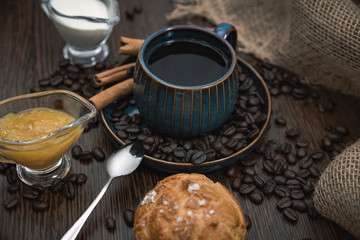 cup of coffee with cinnamon sticks, orange jam, milk and bun on brown table