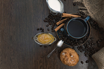 cup of coffee with cinnamon sticks, orange jam, bun and milk on brown table top view