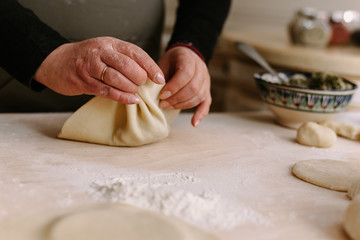 Adult female cook in an apron wraps minced meat in the dough. A woman is cooking khinkali and pinching the dough