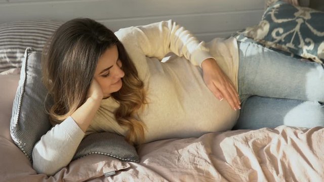 Beautiful mother lying on sofa and tenderly caressing her tummy, slow-motion
