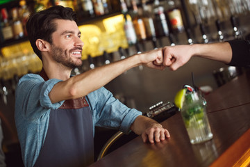 Professional Occupation. Bartender standing at counter serving mojito fist bump to customer smiling friendly