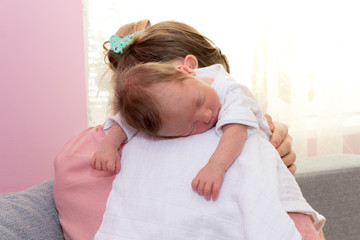 Happy baby girl sleeping on mother shoulder. Loving mother hold baby to burp after breastfeeding....