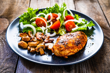 Roast chicken breast and vegetables on wooden background