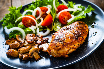 Roast chicken breast and vegetables on wooden background