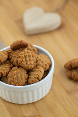 Very tasty peanut butter biscuits on bamboo wooden board in white baking bowl and decorative wood heart, golden baked healthy