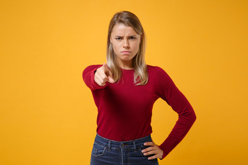 Strict dissatisfied young blonde woman girl in casual clothes posing isolated on yellow orange background studio portrait. People lifestyle concept. Mock up copy space. Point index finger on camera.