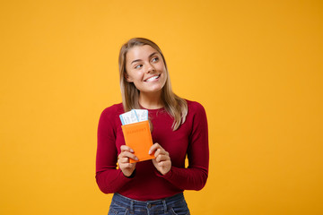 Smiling pensive young blonde woman girl in casual clothes posing isolated on yellow orange background in studio. People lifestyle concept. Mock up copy space. Hold passport tickets, looking aside up.