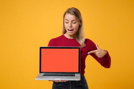 Excited young woman girl in casual clothes posing isolated on yellow orange background. People lifestyle concept. Mock up copy space. Point index finger on laptop pc computer with blank empty screen.