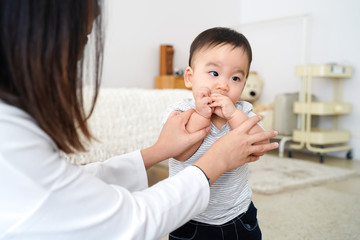 Asian innocent baby boy sucking his own thumb and finger in living room at home. Mom is trying to...