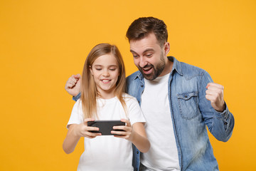 Joyful bearded man with cute child baby girl. Father little kid daughter isolated on yellow background. Love family day parenthood childhood concept. Play game with mobile phone, doing winner gesture.