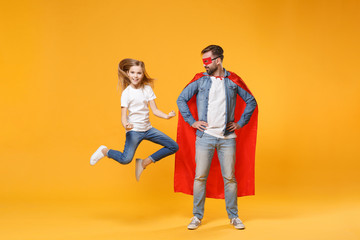 Bearded man in casual clothes Superman costume with child baby girl. Father little kid daughter isolated on yellow background. Love family parenthood childhood concept. Stand with arms akimbo jumping.