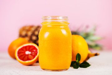 Close up is a jar of fresh yellow smoothie made from natural fruit on a pink background.