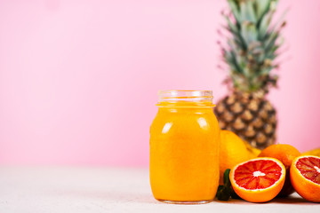 Close up is a jar of fresh yellow smoothie made from natural fruit on a pink background.