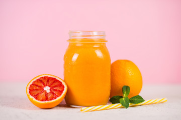 Close up is a jar of fresh yellow smoothie made from natural fruit on a pink background.