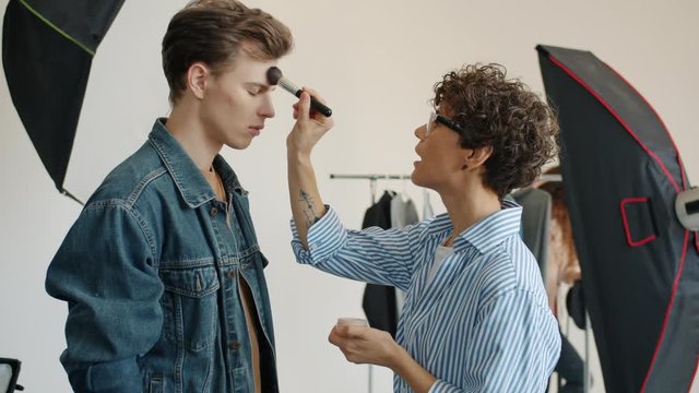 Slow motion of make-up artist beautifying male model in photo studio on white background, stylist with fashionable clothing is visible. People and advertising concept.