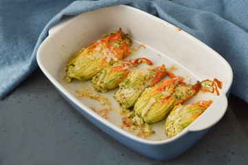 stuffed zucchini or courgette flowers baked with parmesan cheese and parsley garnish in a casserole dish with a blue napkin, copy space