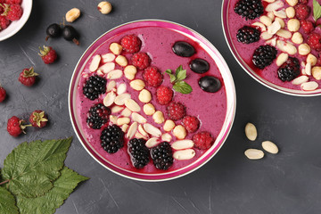 Healthy breakfast smoothie bowl with raspberries, blackberries, currants, peanuts and hazelnuts on a dark background, Top view