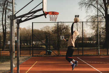 Street basketball player having training outdoor. He is making a good action. Basketball slam dunk.