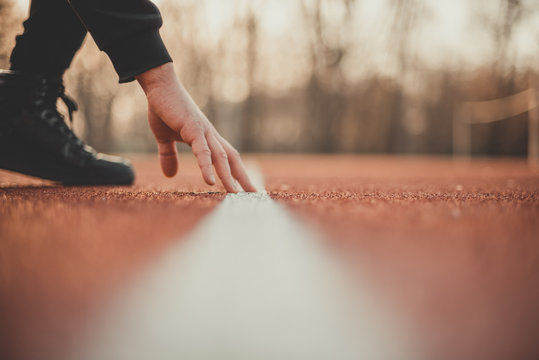 Young athlete preparing at start line and making starting. Single track and field sprinter in a stadium starting out. Close detail of track runner putting hands at starting line.