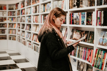 Portrait of a beautiful blonde woman looking for a book in store