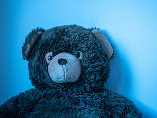 'Feeling blue' -A huge teddy bear leaning at wall with blue light.